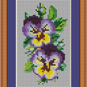 May include: Cross-stitch artwork of pansies in shades of purple, yellow, and green, set against a gray background. The framed piece features a wooden frame and a blue mat. The text "PuntAGOpettitePatternetsycom" is visible at the bottom.
