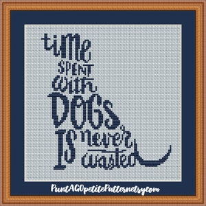 Könnte beinhalten: Ein Kreuzstichmuster auf hellblauem Stoff mit dunkelblauem Text, der lautet: time SPENT WITH DOGS Is never wasted. Der Text ist in der Form eines sitzenden Hundes angeordnet. Das Design ist von einem dunkelblauen Rand und einem Holzrahmen umgeben.