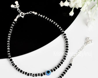 May include: A silver anklet with black beads and a blue evil eye charm. The anklet has a silver chain with two small bells at the end.