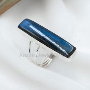 May include: A silver ring featuring a blue labradorite gemstone. The ring has a distinctive design with multiple bands.