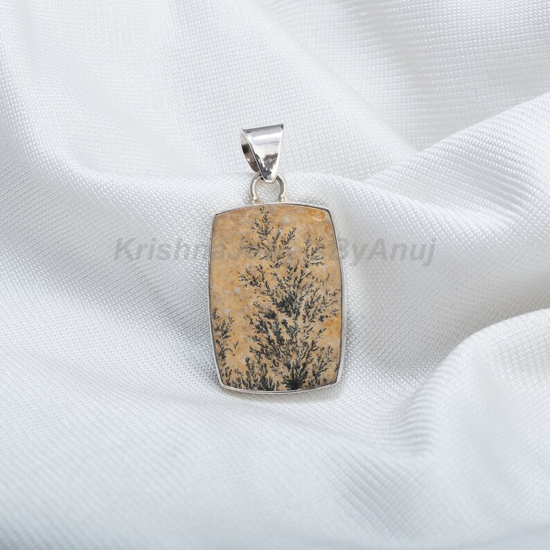 May include: A silver pendant featuring a rectangular, light brown stone with a black dendritic agate tree pattern.