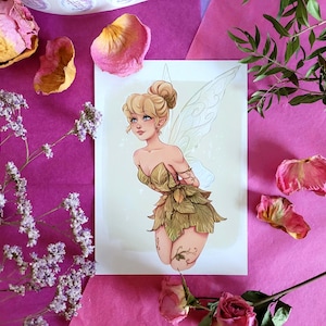 Può includere: Una stampa di una fata con capelli biondi e abiti di foglie verdi. La fata ha grandi ali dettagliate. La stampa è circondata da petali di rosa rosa, fiori secchi e verde su uno sfondo rosa.