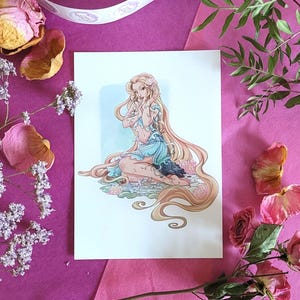 Peut inclure: Une impression d'une femme aux longs cheveux blonds et tatouages, v&ecirc;tue d'une robe bleue. L'&oelig;uvre est entour&eacute;e de fleurs et de feuillages roses et violets, sur un fond rose.