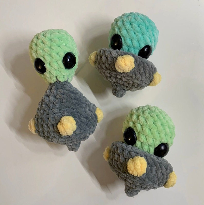 Pu&ograve; includere: Tre giocattoli di peluche all'uncinetto a forma di alieni. Ogni alieno ha una testa verde e un corpo grigio. Gli alieni hanno grandi occhi neri e accenti gialli.