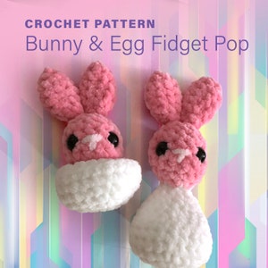 Pode incluir: Dois brinquedos de crochet para fidget em forma de coelho e ovo. O coelho é rosa com detalhes brancos e olhos pretos. O ovo é branco. Os brinquedos estão sobre um fundo colorido.