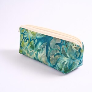 May include: A rectangular pencil case with a cream-colored zipper and a vibrant teal and green floral pattern. The case is made of fabric and is designed to hold pens, pencils, and other stationery items.