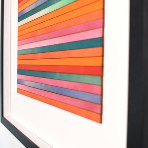 May include: A framed abstract art piece with horizontal stripes of various colors, including orange, pink, blue, and green.