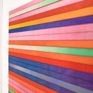 May include: A framed artwork featuring a colorful abstract design. The artwork is made up of horizontal stripes of various colors, including red, orange, yellow, green, blue, and purple. The stripes are arranged in a gradient pattern, with the lighter colors at the top and the darker colors at the bottom.