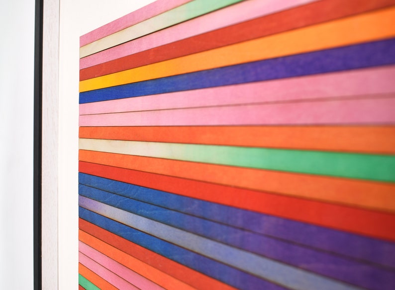 May include: A framed artwork featuring a colorful abstract design. The artwork is made up of horizontal stripes of various colors, including red, orange, yellow, green, blue, and purple. The stripes are arranged in a gradient pattern, with the lighter colors at the top and the darker colors at the bottom.