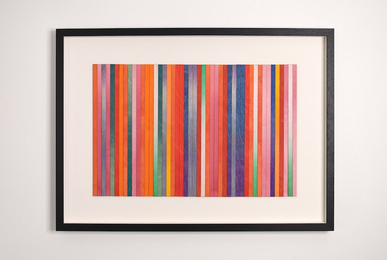 May include: A framed artwork featuring a colorful abstract design. The artwork is made up of vertical stripes of various colors, including red, orange, yellow, green, blue, purple, and pink.