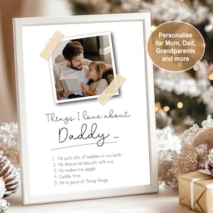 May include: A white framed print featuring a photograph of an adult and a child reading a book, attached with tape. The text reads: Things I love about Daddy... followed by a numbered list of five points describing positive shared activities.