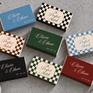 May include: A collection of rectangular matchboxes in various colors and patterns. Some feature a solid color with the text Olivia & Ethan 09.18.26, while others display a checkered pattern with the text The Perfect Match.