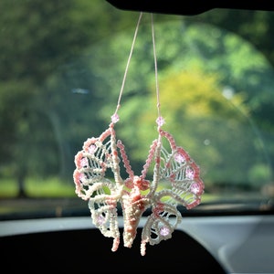 May include: A white and pink butterfly-shaped car charm with pink beads hanging from a string.