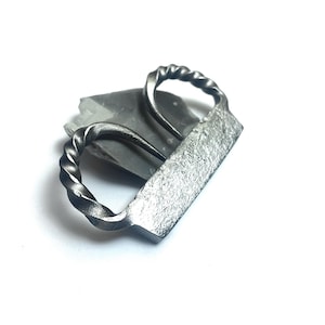 Peut inclure: Décapsuleur en métal forgé à la main. Il présente un corps rectangulaire texturé et une poignée torsadée. Le décapsuleur est de couleur gris foncé et semble être en fer ou en acier. La poignée a un design décoratif en forme de corde.