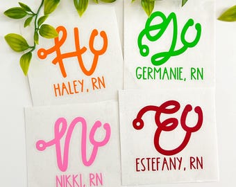 May include: Four white square decals featuring stethoscope-shaped letters in orange, green, pink, and red. The text reads HALEY, RN in orange, GERMANIE, RN in green, NIKKI, RN in pink, and ESTEFANY, RN in red, each styled with a stethoscope motif.