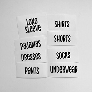 May include: A set of white rectangular labels with black text featuring the words LONG SLEEVE, SHIRTS, PAJAMAS, SHORTS, DRESSES, SOCKS, PANTS, and UNDERWEAR arranged in two columns. The labels have a clean, sans-serif font and are organised for clothing organisation.