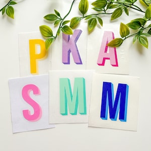 May include: A set of six colourful letters spelling out "PKASMM" on a white background. The letters are made of paper and have a 3D effect. The letters are in the colours yellow, purple, pink, green, and blue.