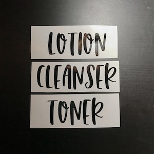 May include: Three rectangular white vinyl labels featuring black lettering in a script font. The labels display the words LOTION, CLEANSER, and TONER, each on a separate strip, designed for application onto skincare containers or bathroom bottles.