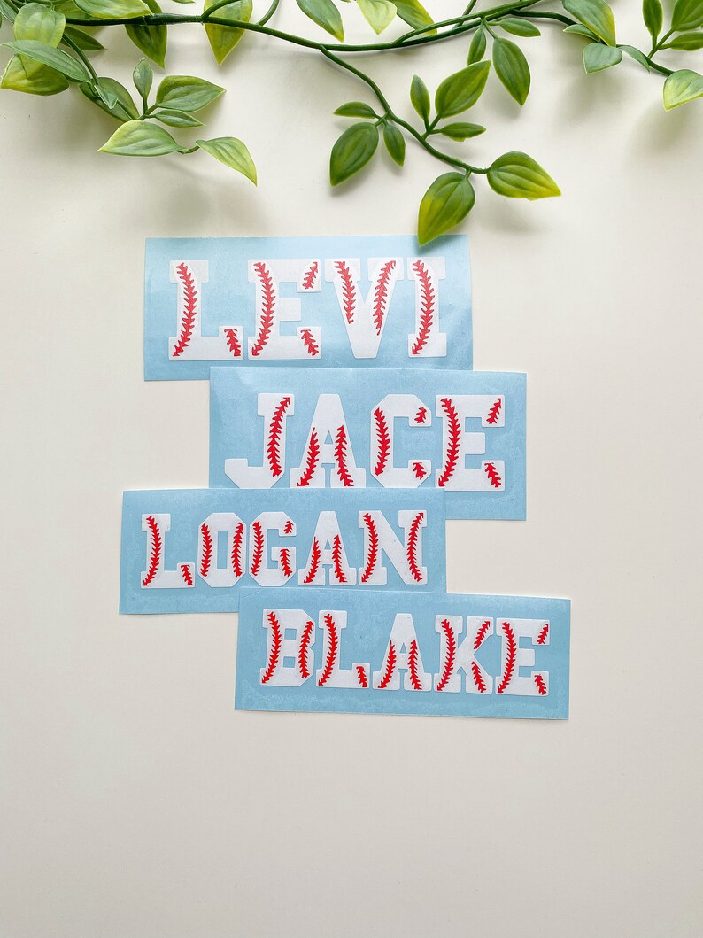 May include: Four blue and white baseball-themed name decals with red stitching. The names are Levi, Jace, Logan, and Blake.