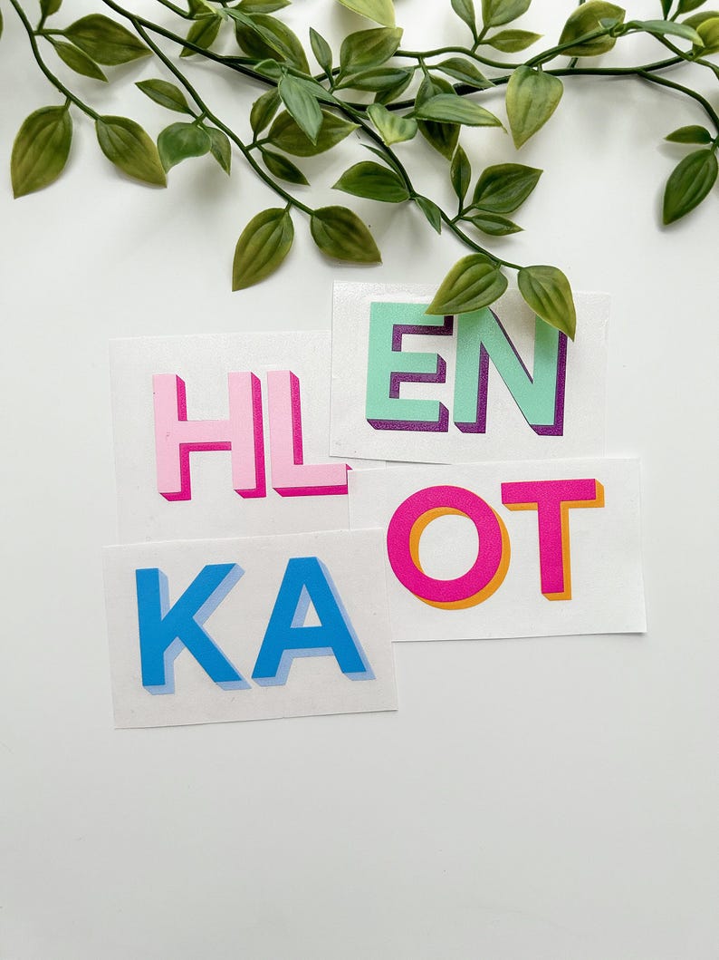 May include: A set of rectangular stickers featuring bold, block-style letters. The stickers display the characters HL, EN, KA, and OT in vibrant colors including pink, mint green, blue, and magenta, each with a distinct drop shadow effect.