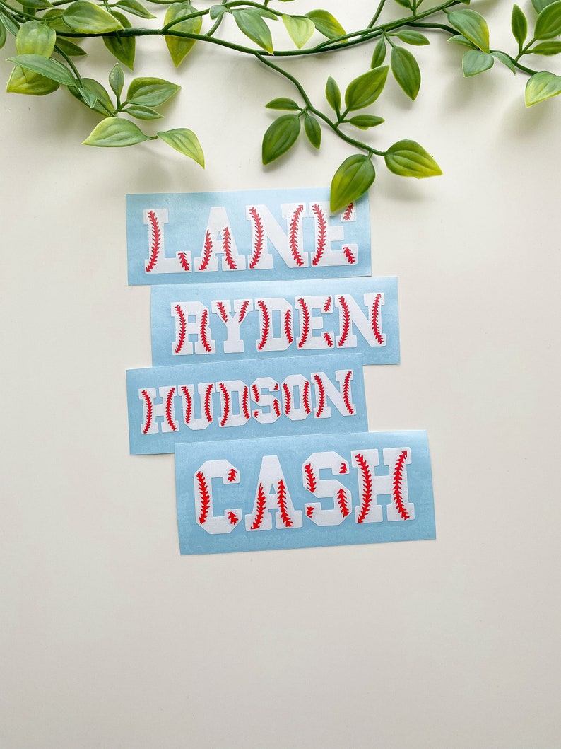 May include: Four white vinyl decals with red baseball stitching. The names "Lane", "Ryden", "Hudson", and "Cash" are spelled out on each decal.