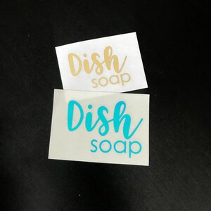 May include: Two rectangular adhesive vinyl decals featuring the text Dish soap in a script and sans-serif font combination. One decal displays the text in a metallic gold finish, while the other decal displays the text in a bright cyan blue color.