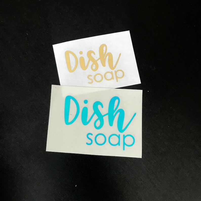 May include: Two rectangular adhesive vinyl decals featuring the text Dish soap in a script and sans-serif font combination. One decal displays the text in a metallic gold finish, while the other decal displays the text in a bright cyan blue color.
