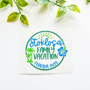 Puede incluir: Una pegatina circular con el texto Stoklosa FAMILY VACATION FLORIDA 2023 en azul y verde. El dise&ntilde;o incluye un sol verde, dos palmeras verdes y una flor de hibisco azul, todo encerrado dentro de un borde circular de color verde.