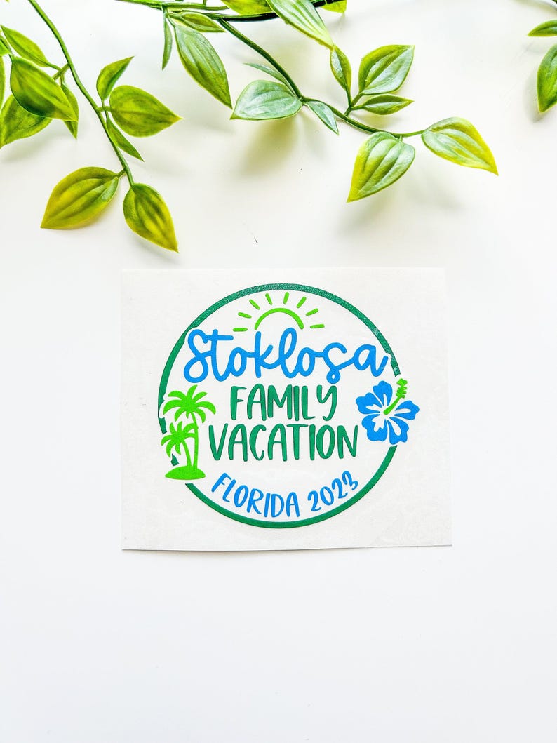 Puede incluir: Una pegatina circular con el texto Stoklosa FAMILY VACATION FLORIDA 2023 en azul y verde. El dise&ntilde;o incluye un sol verde, dos palmeras verdes y una flor de hibisco azul, todo encerrado dentro de un borde circular de color verde.