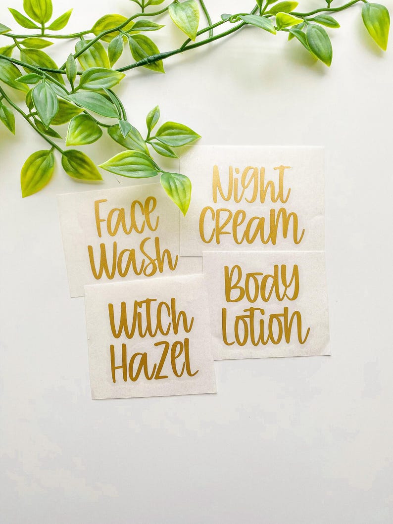 May include: Four square adhesive labels with metallic gold cursive lettering on a white backing. The labels feature the text Face Wash, Night Cream, Witch Hazel, and Body Lotion, arranged in a cluster with a green leafy vine at the top.