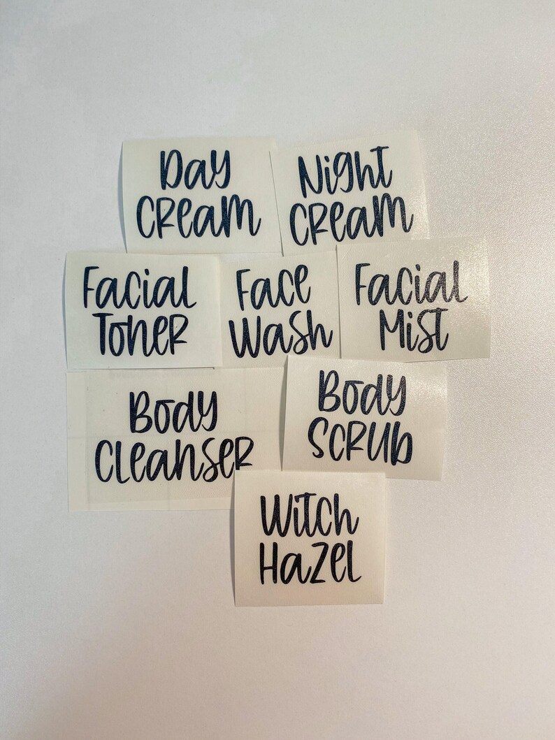 May include: A collection of seven individual black vinyl adhesive labels with white backing, featuring the text: Day Cream, Night Cream, Facial Toner, Face Wash, Facial Mist, Body Cleanser, Body Scrub, and Witch Hazel in a handwritten script font.