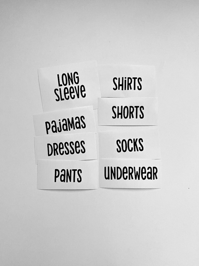 May include: A set of white rectangular labels with black text featuring the words LONG SLEEVE, SHIRTS, PAJAMAS, SHORTS, DRESSES, SOCKS, PANTS, and UNDERWEAR arranged in two columns. The labels have a clean, sans-serif font and are organised for clothing organisation.