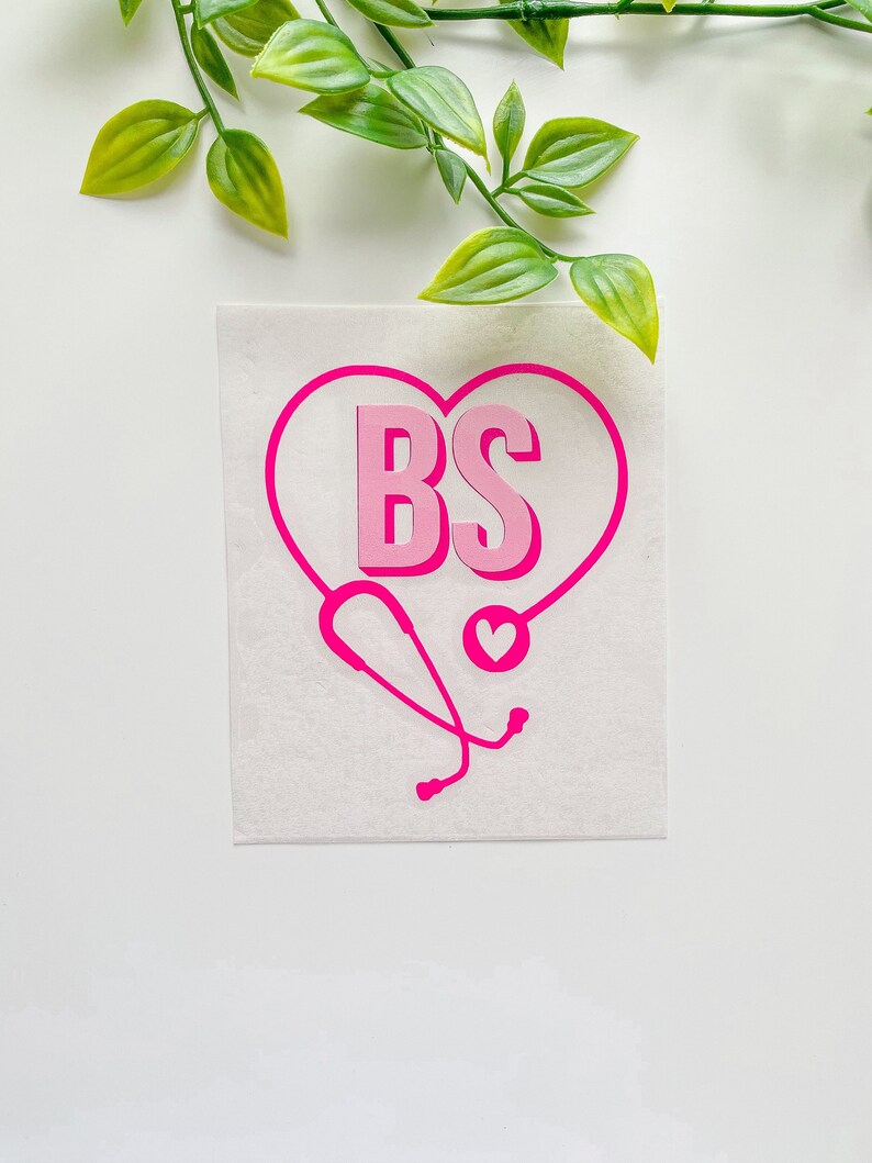 Peut inclure: Autocollant en vinyle rose avec les lettres "BS" &agrave; l'int&eacute;rieur d'un c&oelig;ur, avec un st&eacute;thoscope rose et un petit c&oelig;ur en bas.