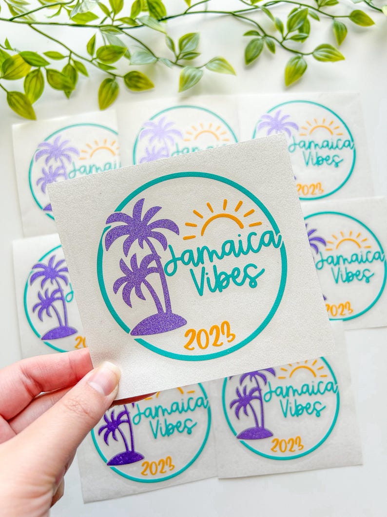 Puede incluir: Una pegatina cuadrada con un borde circular turquesa, una palmera de purpurina morada, un sol amarillo y el texto "Jamaica Vibes 2023" en letra cursiva turquesa. El dise&ntilde;o est&aacute; impreso sobre un soporte blanco, con varias pegatinas id&eacute;nticas visibles.