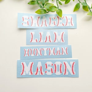 May include: Four blue and white baseball-themed name decals with red stitching. The names are "Swagger", "Liam", "Huntman", and "Mason".