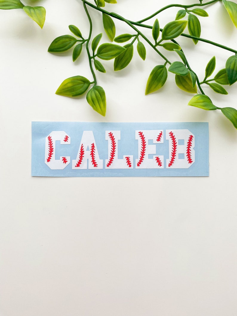 May include: A white vinyl sticker with the name "CALEB" in red baseball stitching.