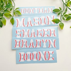 May include: Five white vinyl stickers with baseball stitching designs. The names "BOONE", "BRADYN", "SWAGER", "MASON", and "HUNTER" are spelled out on the stickers.