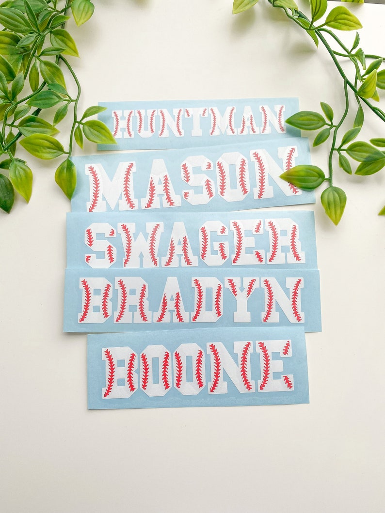May include: Five white vinyl stickers with baseball stitching designs. The names "BOONE", "BRADYN", "SWAGER", "MASON", and "HUNTER" are spelled out on the stickers.