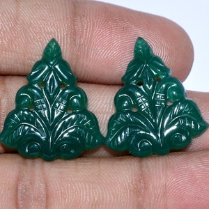 May include: Two green carved gemstone pendants in the shape of a stylized tree. The pendants have intricate details and are perfect for jewelry making.