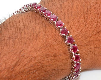 May include: A silver bracelet featuring a series of oval-cut, vibrant red gemstones. The gemstones are set closely together, creating a continuous line of color. The bracelet is shown on a wrist.