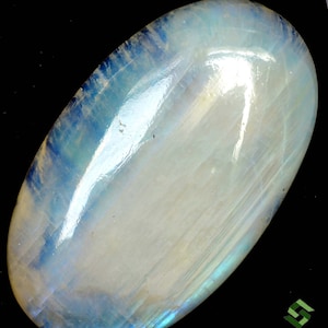 Puede incluir: Un cabujón de piedra lunar grande, de forma ovalada, de color blanco lechoso con destellos iridiscentes azules y verdes. La piedra es lisa y pulida.