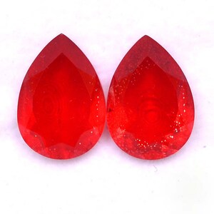 May include: Two red pear-shaped glass beads with a faceted design.
