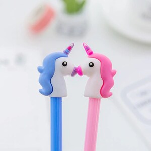 May include: Two unicorn-shaped pens, one blue and one pink, with white faces and pink lips, are positioned as if they are kissing.
