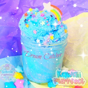 May include: A clear glass jar filled with blue slime with a rainbow and star sprinkles. The jar has the text "Dream Catcher" written on it. The slime is surrounded by pastel blue and purple tissue paper and white stars.