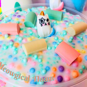 May include: A white slime with colorful sprinkles and a small white unicorn figurine. The slime is in a clear plastic container with the text "Meowgical Foam" written on the bottom.