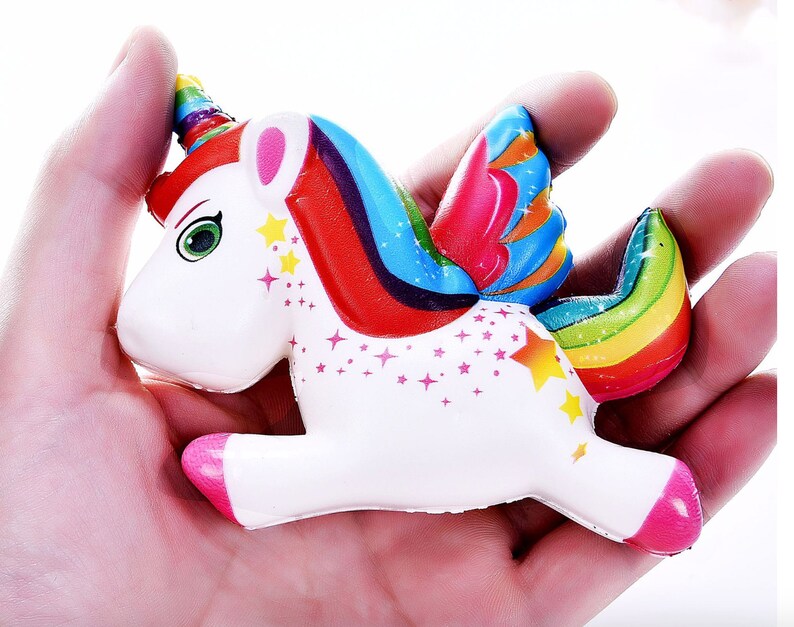 May include: A white unicorn squeeze toy with a rainbow mane, tail, and wings. The unicorn has a pink nose and hooves, and is decorated with small white stars.