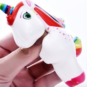 May include: A white unicorn squeeze toy with a rainbow mane and tail. The unicorn has a pink nose and green eyes. The toy is made of soft, squishy material.