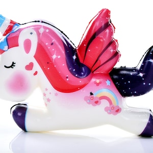 Puede incluir: Un juguete de unicornio blanco con mejillas rosadas, un cuerno a rayas y alas coloridas. Las alas son rojas y rosas con un dise&ntilde;o de estrellas. Un arco&iacute;ris y nubes est&aacute;n en el costado. El unicornio tiene una cola y pezu&ntilde;as moradas.