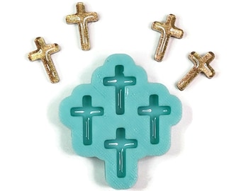 May include: A light blue silicone mold with five cross shapes. The mold is surrounded by five gold glitter crosses.
