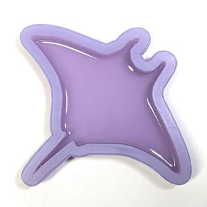 May include: A lilac-coloured, manta ray-shaped mould with a glossy finish. The mould has a raised border and a smooth, flat interior. The design is a stylized representation of a manta ray.